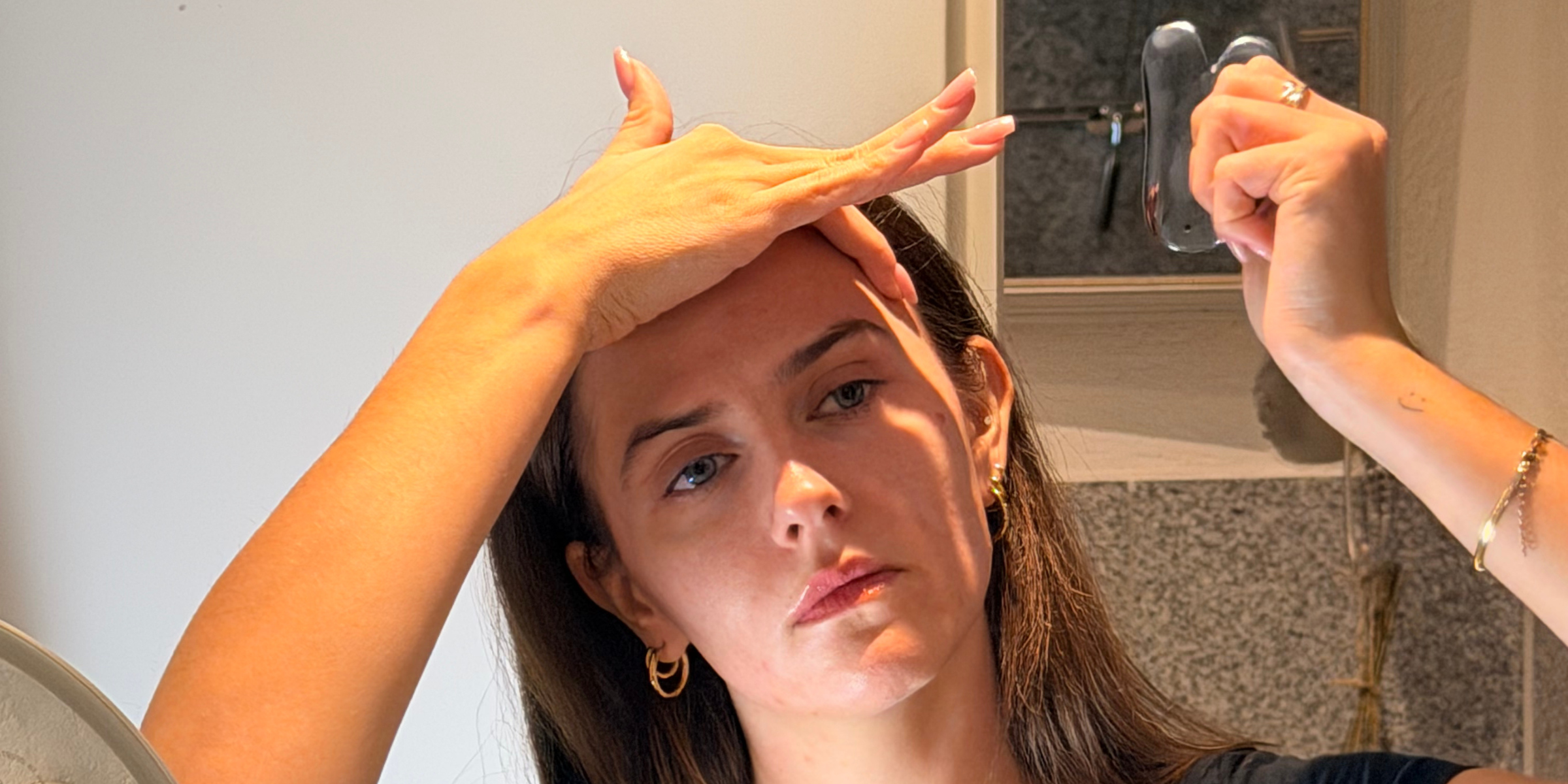 Person führt eine Gua-Sha-Anwendung im Gesicht vor dem Spiegel durch, hält den TERAGLOW Gua Sha an der Stirn; ruhige Badezimmeratmosphäre mit sanftem Licht und Fokus auf die Technik.