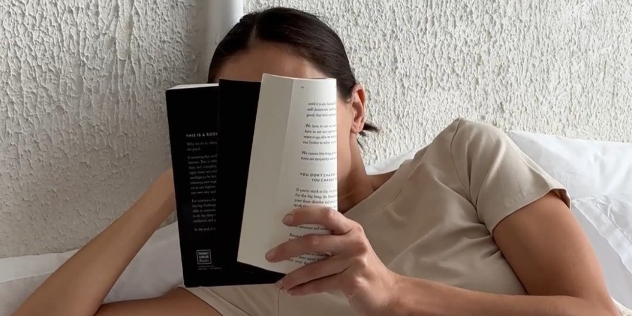 Dunkelhaarige Frau die ein Buch liest während Sie im Bett liegt