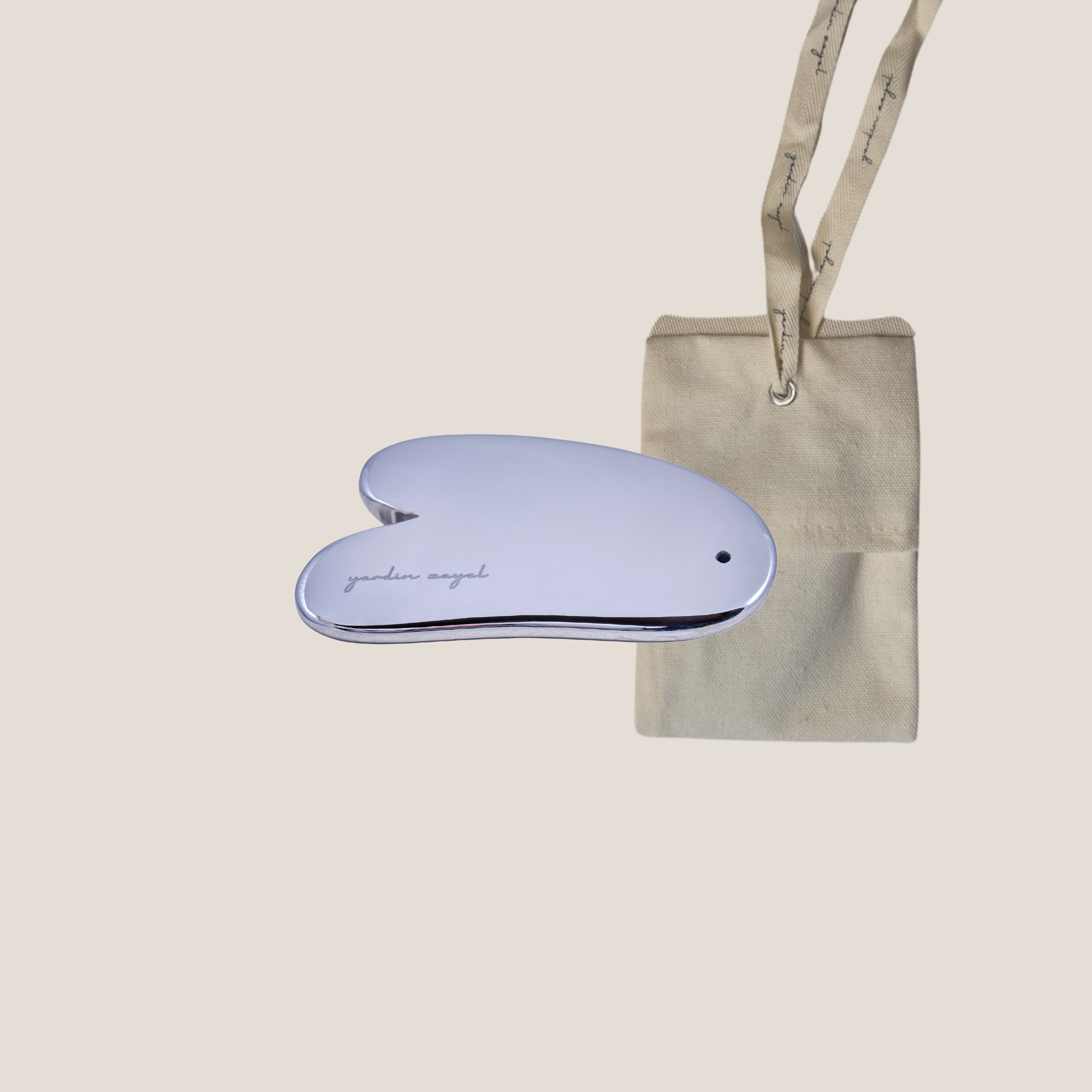 Flatlay: yardin zayel Gua Sha Teraglow aus Terahertz-Material mit zugehöriger Baumwolltasche.