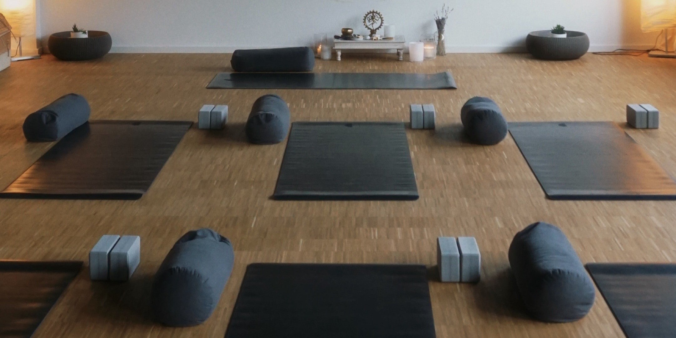 aufgereihte Yogamatten in einem Studio mit Bolstern und Yogablöcken nebendran 
