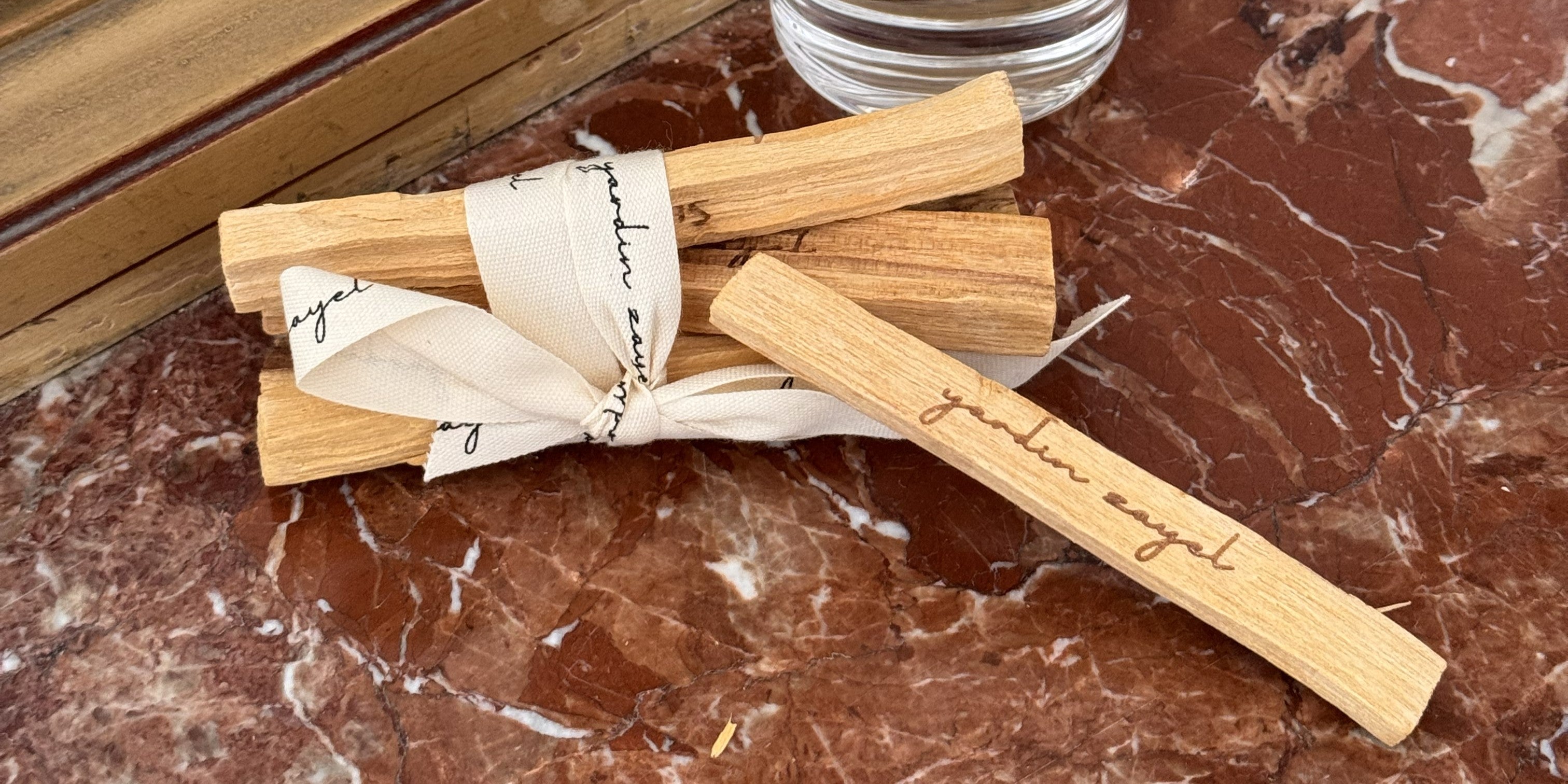 Palo Santo Bundle mit einen herausfallenden Palo Santo Stick auf einer Marmorplatte mit einer geschwungenen Kerze im Hintergrund
