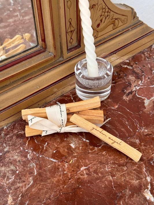 Palo Santo Bundle mit einen herausfallenden Palo Santo Stick auf einer Marmorplatte mit einer geschwungenen Kerze im Hintergrund