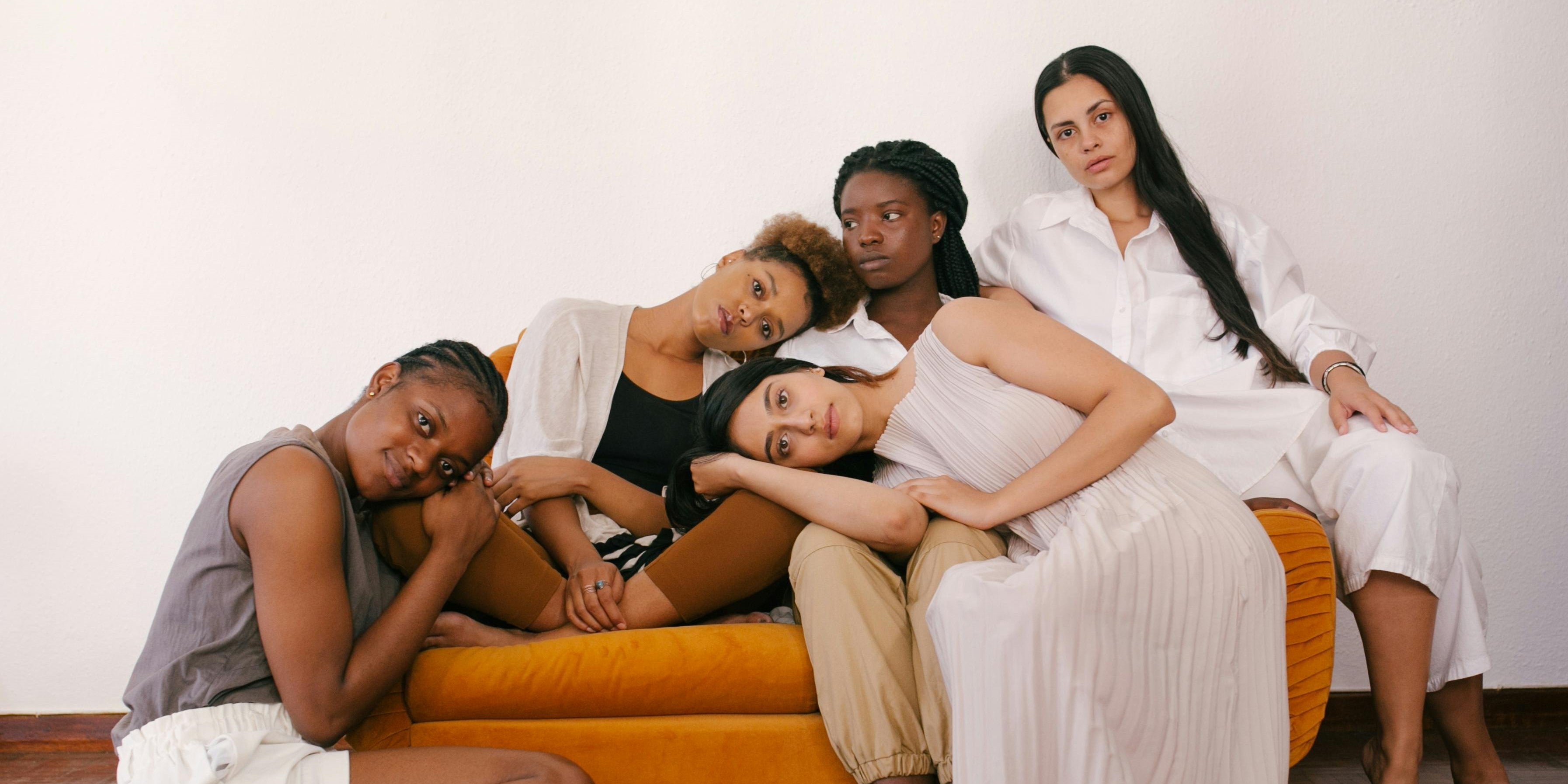 5 Frauen verschiedener Ethnien, die auf einem Sofa zusammensitzen